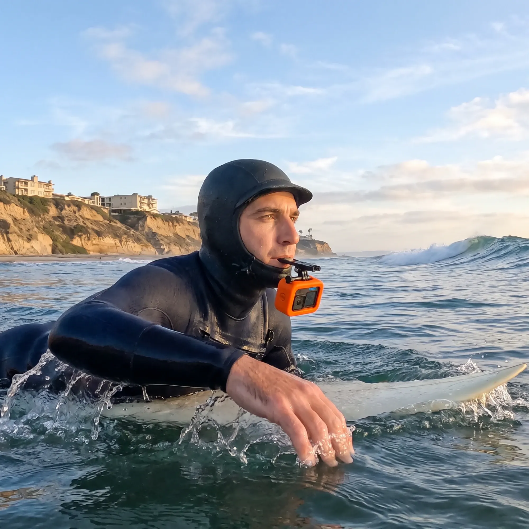 A surfer paddling out, biting down on a mouth mount that holds an action camera